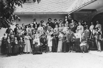 A golden wedding celebrated by the family locally known as Jurčkovi in Trnje near Škofja Loka, 1904–1909. The couple celebrating the golden wedding anniversary and some guests are clad in national costumes. The person standing in the back row, next to the lamp, is the painter Ivan Grohar from Sorica. 